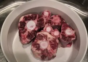 Washed and sliced uncooked oxtails in a white bowl for Single Ingredient Groceries.