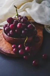 Fresh red grapes in a wooden bowl on a wooden platter with white cloth.