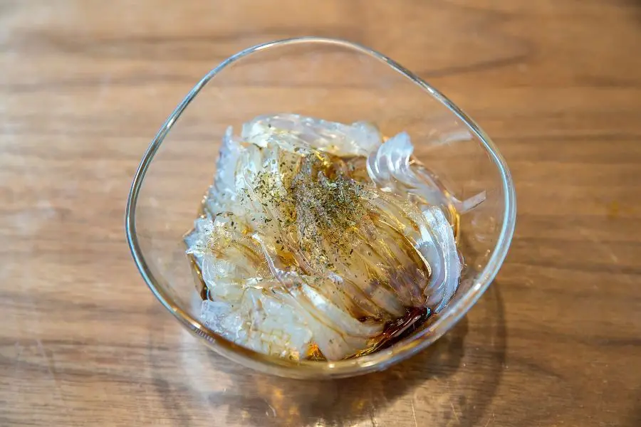KONJAC NOODLES WITH SEASONING AND SOY SAUCE IN CLEAR GLASS BOWL ON WOODEN SURFACE