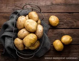 Photograph of potatoes in a wire basket with a grey linen cloth and on a brown wood table.