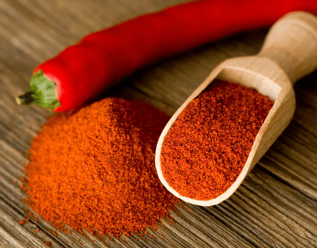paprika powder in a spoon with a pepper on a table