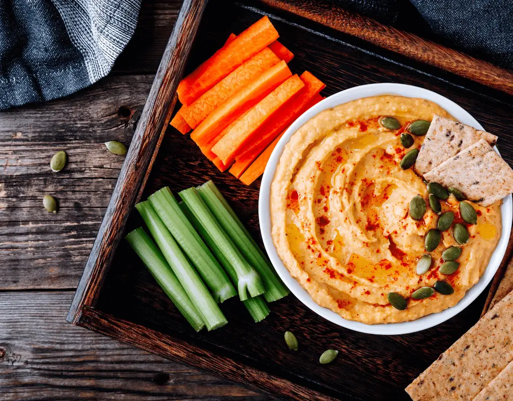 preparaed hummus in a white bowl with celery sticks