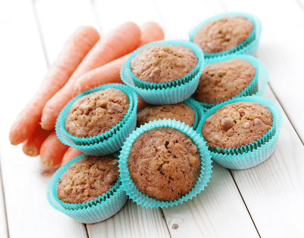 carrot muffins displayed with carrots on a white wood background