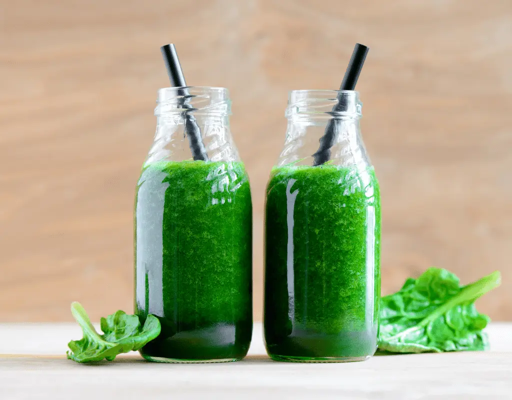 green vegetable smoothies in glass bottles with black straws