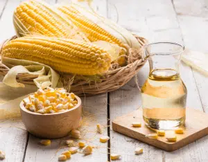 corn on the cob and corn oil in a clear bottle on a wooden background