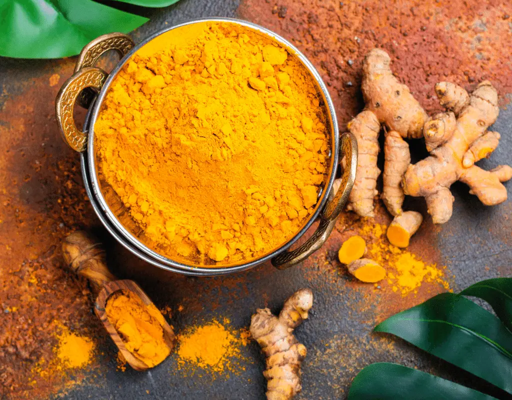 Turmeric powder in a bowl with turmeric root displayed on a dark background