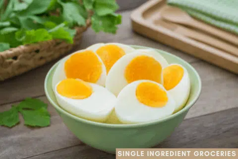 Sliced hard boiled eggs in a green bowl on a wooden table with a cutting board and cilantro in the background. Blog image about egg allergy for Single Ingredient Groceries. 