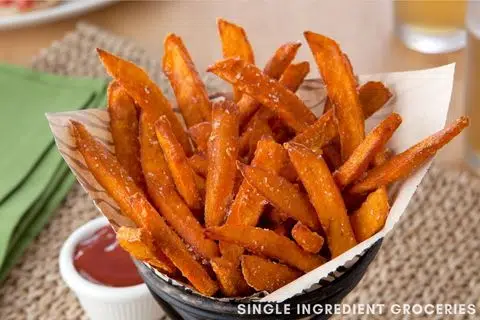 Sweet Potato Fries standing upright in a serving container on a brown and green placemat with salt and a container of tomato ketchup for Single Ingredient Groceries blog.