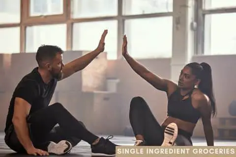 Man and woman sitting on gym floor wearing athletic clothes reaching up to give a high five. For Single Ingredient Groceries blog post about Black Ginger Extract. 