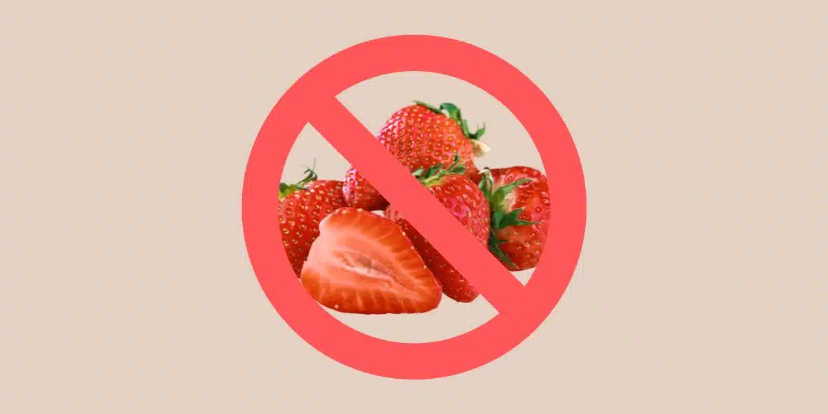 Whole and sliced red strawberries on tan background behind a red prohibited symbol (circle with a line) for Single Ingredient Groceries blog post about strawberry allergy.