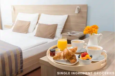 Strawberries as part of a fruit cup served with coffee and breakfast next to a hotel bed for an image about breakfast in bed and strawberry allergy. 