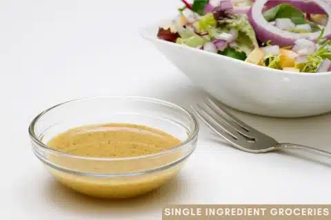 Salad with red onions, and lettuce in a white bowl with a for and small clear dish of salad dressing for Single Ingredient Groceries blog post about white balsamic vinegar. 